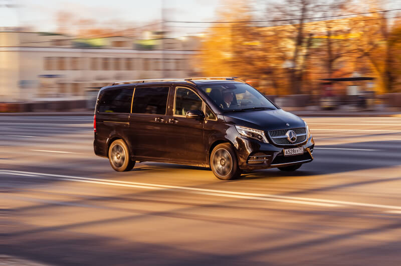 Mercedes Minivan driving down a city road providing luxury chauffeur services